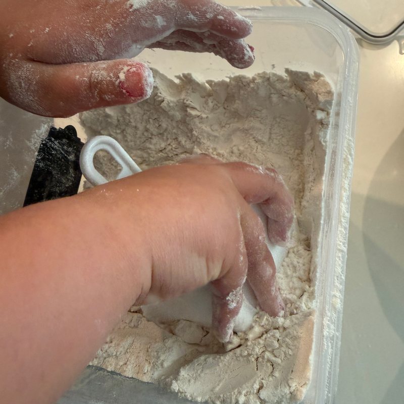 Little hands reaching into the flour bin to fill a measuring cup