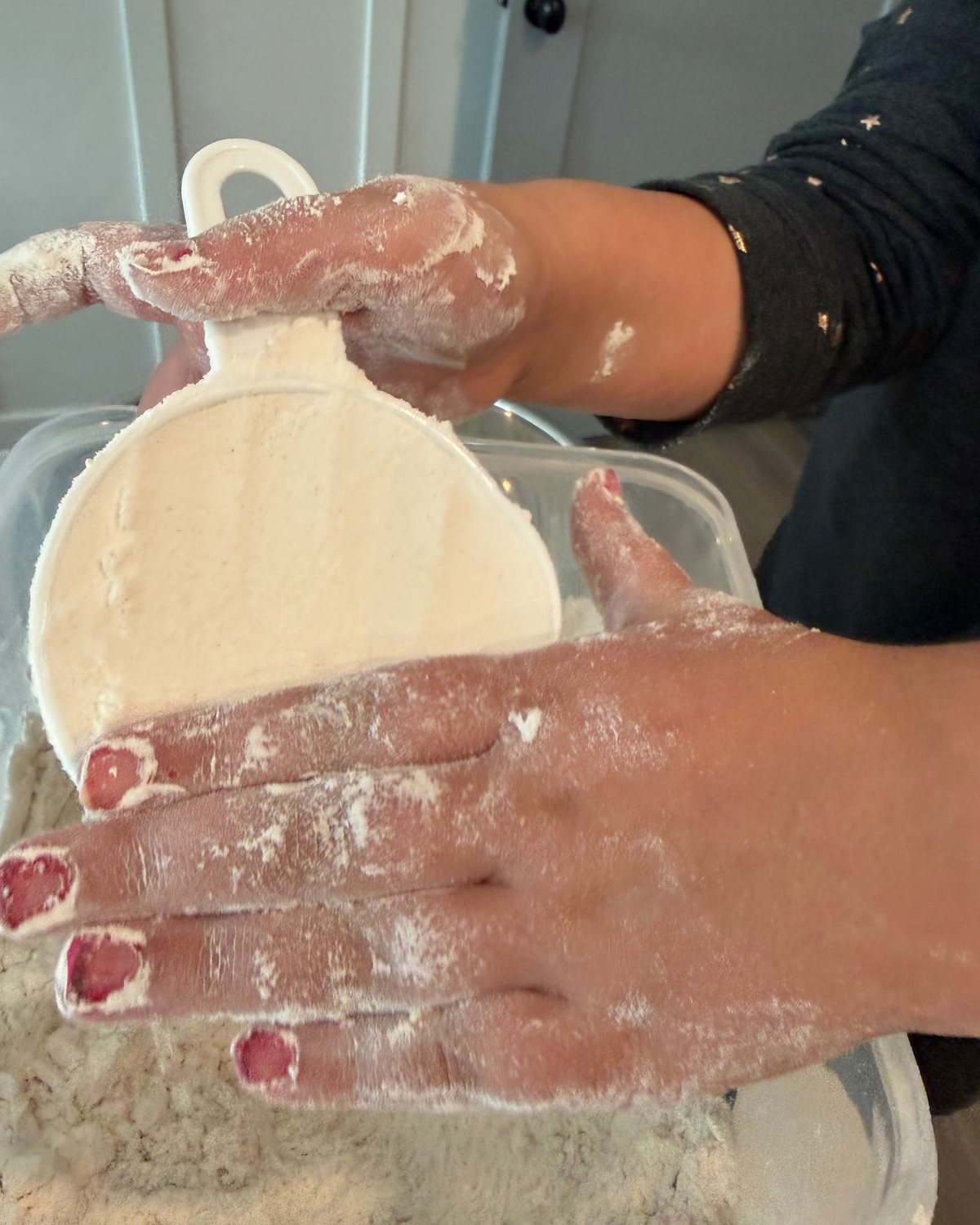 A young baker's flour-dusted hands leveling a scoop of flour over the flour bin